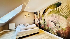 Ein Schlafzimmer mit schrägem Dach, einem Bett, einem Heizkörper und einer großen Wandmalerei.