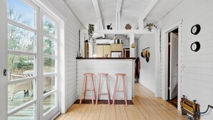A kitchen with a wooden floor, white walls, and a bar area with stools.