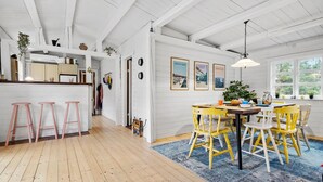 A bright kitchen with wooden floors, a dining area with yellow chairs, and a large window with a view.