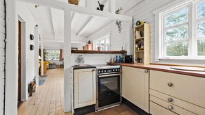 A kitchen with a stove, oven, and wooden cabinets. There is a window with a view of trees.