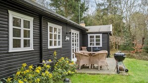 A wooden cabin with a deck, wicker furniture, and a barbecue grill.