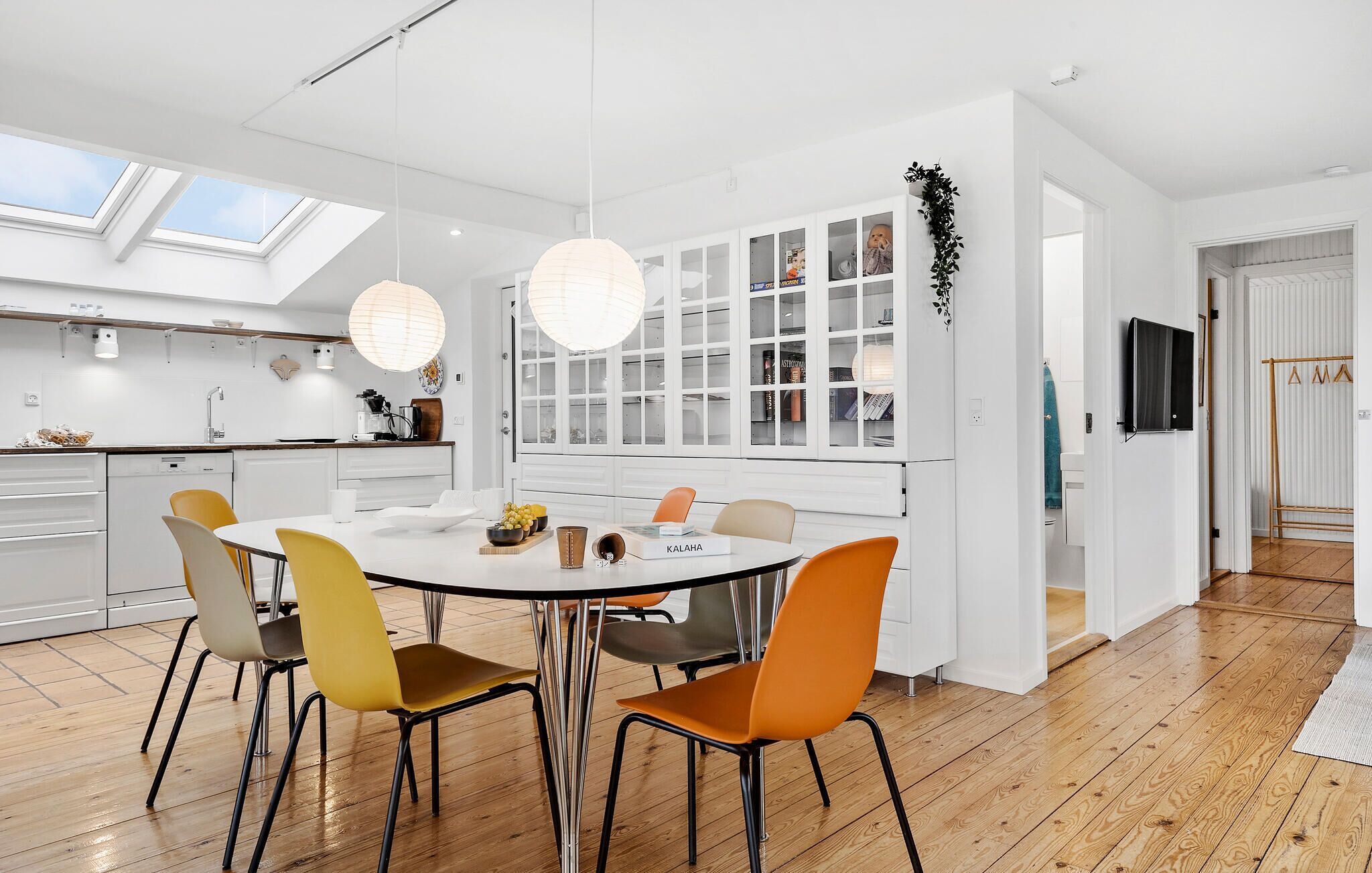 A modern kitchen with a central island, white cabinetry, and a dining area with orange chairs.