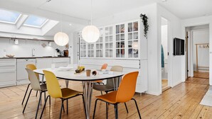A modern kitchen with a central island, white cabinetry, and a dining area with orange chairs. - 3 bedroom amazing home in Otterup (Otterup)