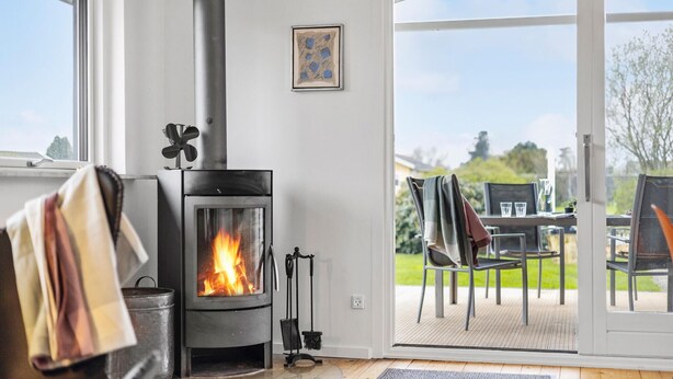 A modern living room with a wood-burning stove, a dining area with outdoor seating, and a large window offering a view of the outdoors. - 3 bedroom amazing home in Otterup (Otterup)
