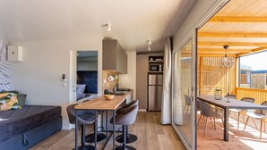 A modern kitchen with a wooden table and bar stools, a refrigerator, and a microwave.