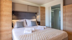 A modern hotel room with a large bed, wooden headboard, and a glass shower enclosure.