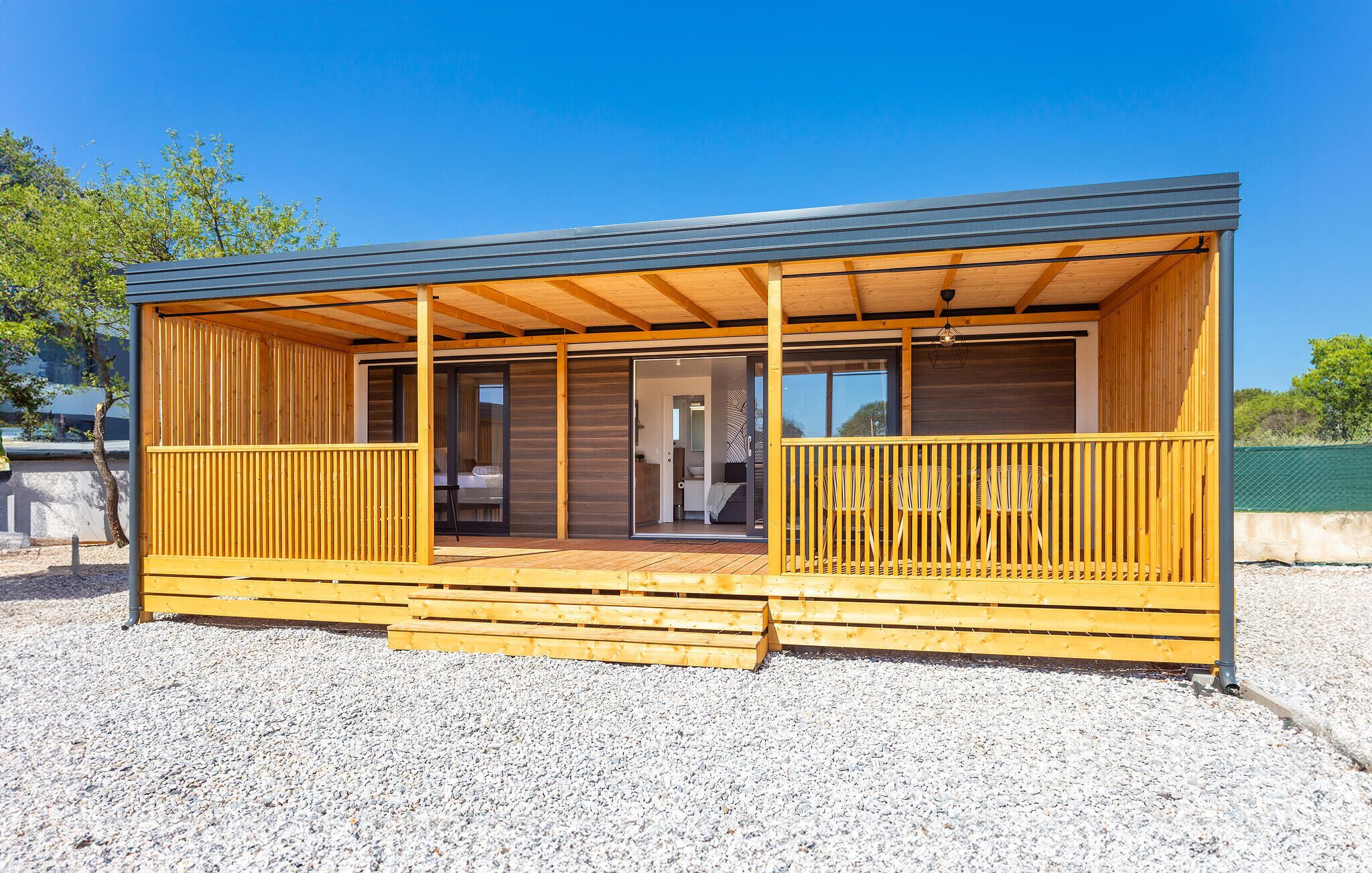 A modern, single-story wooden cabin with a covered porch and sliding glass doors leading to an interior with a bed and seating area.