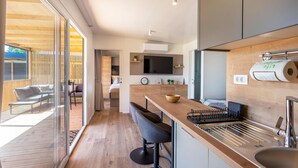 A modern kitchen with a wooden countertop, bar stools, a built-in oven, and a large window overlooking a deck.