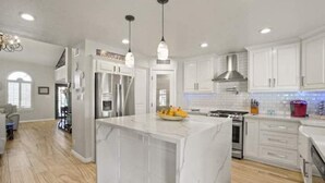 A modern kitchen with white cabinetry, a marble island, stainless steel appliances, and pendant lighting. - Resort Style Vacation Home (El Paso)