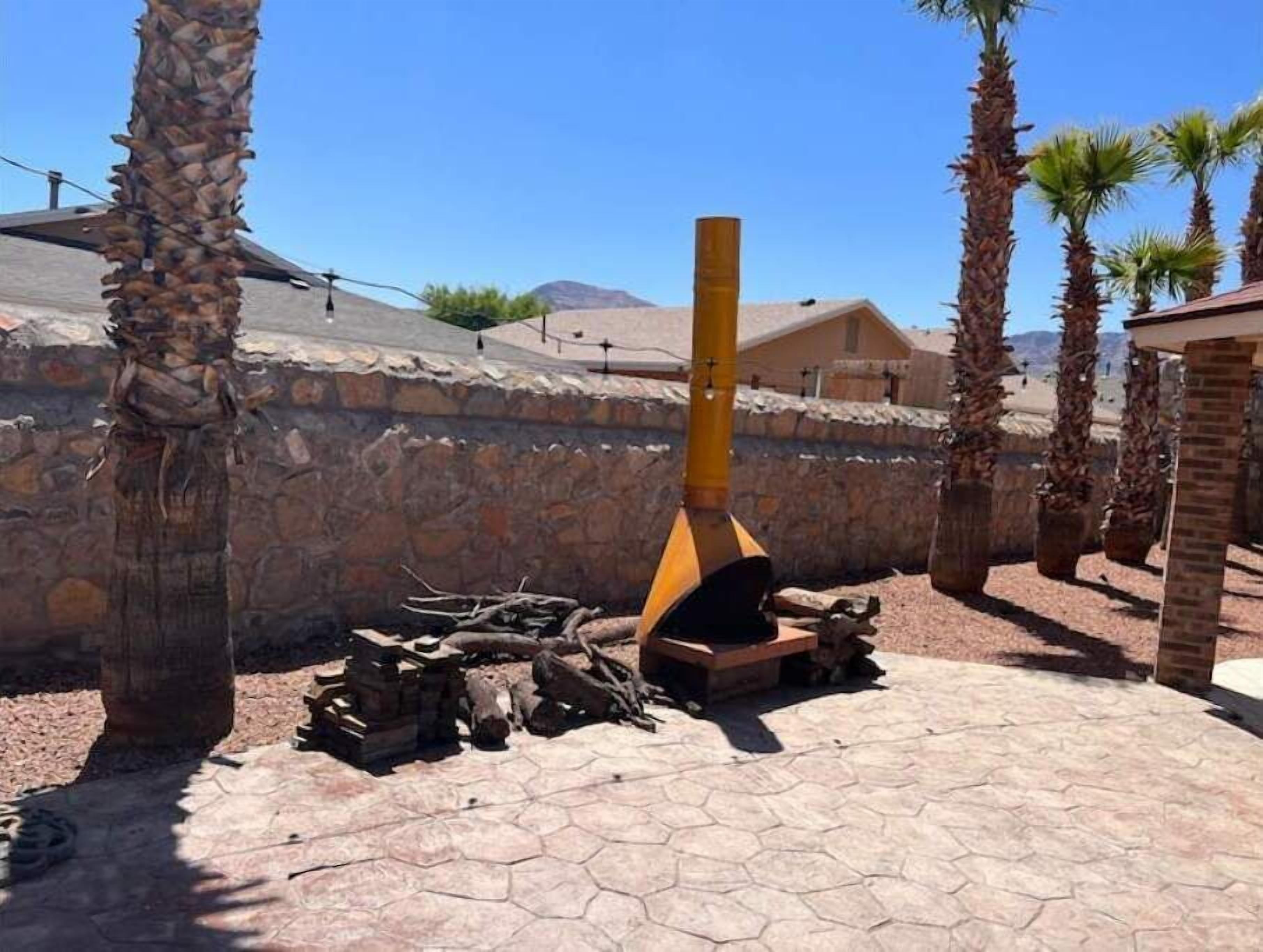 Muro de piedra con una estructura de madera al frente, palmeras y cielo despejado.