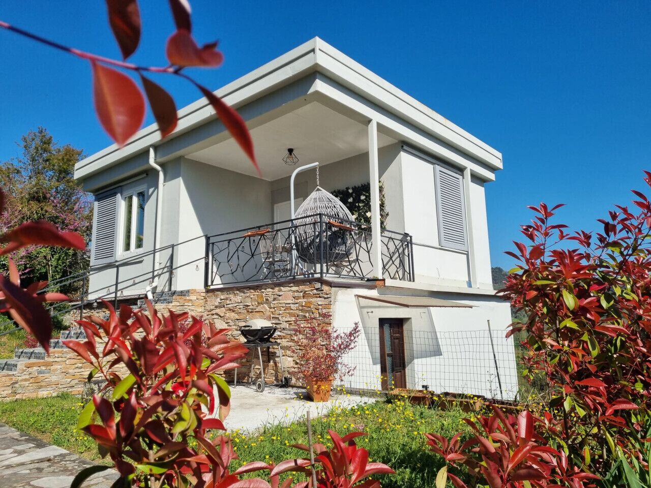Een modern huis met twee verdiepingen, een balkon, stenen fundering en een kleine tuin.