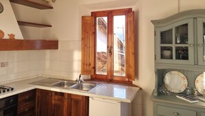 A kitchen with wooden cabinets, a stainless steel sink, and a window with wooden shutters. - La Tegola - Old town apartment with amazing views (Barga)