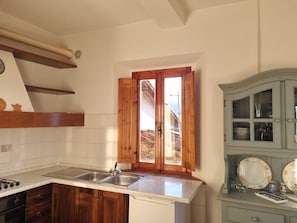 A kitchen with wooden cabinets, a stainless steel sink, and a window with wooden shutters.
