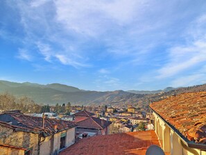 A town with a prominent red-roofed building in the foreground, a clear blue sky, and distant mountains.