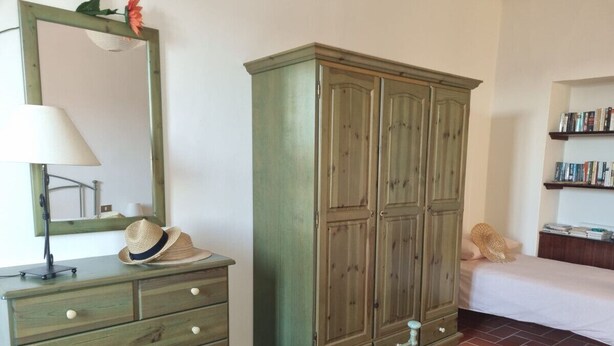 Une chambre à coucher comprenant une commode en bois, une armoire, un lit, une table de chevet avec une lampe et une bibliothèque.