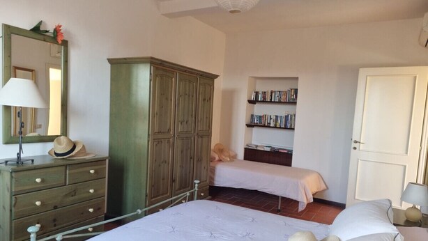 A bedroom with a large bed, a wardrobe, a bedside table with a lamp, a bookshelf, and a door. - La Tegola - Old town apartment with amazing views (Barga)