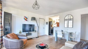 A modern living room with a flat-screen TV, leather sofas, a dining area with a table and chairs, and a kitchen in the background. - Bel appart avec balcon et clim près des Calanques (Marseille)