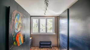 A modern interior with a large abstract painting, a bench, and a window with a view of trees. - Bel appart avec balcon et clim près des Calanques (Marseille)