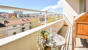 Un balcón con una mesa lista para comer, un aparador de madera y vistas de la ciudad.