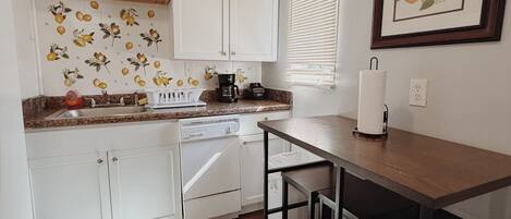 A compact kitchen with white cabinets, a coffee maker, and a dining area with a table and chairs.