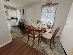 A dining area with a round table set for six, surrounded by wooden chairs with floral upholstery. A patterned rug lies on the floor, and a kitchen is visible in the background. - Valdosta relax getaway (Valdosta)