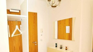 A room with a wooden floor, a white wardrobe, a white console table, a mirror, and a chandelier. - Luxury 1 bedroom flat w parking&balcony (Luxembourg City)