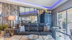 A modern living room with a black leather sofa, a glass coffee table, and a large window with a view of the outdoors. - Dang This Place Fancy / Sonoran Sea / Sandy Beach / Beachfront End Unit (Puerto Peñasco)