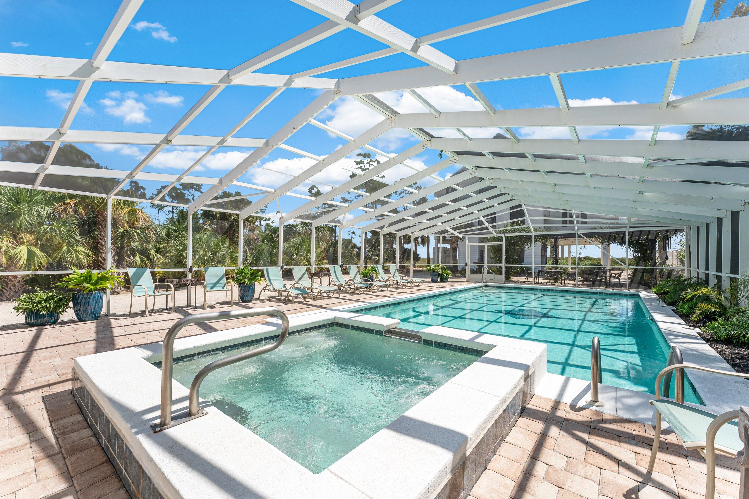 A pool area with a glass ceiling, lounge chairs, and potted plants.