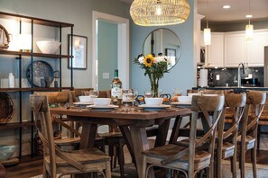 Un comedor con una mesa de madera dispuesta para seis personas, rodeada de sillas de madera. Un jarrón con flores está sobre la mesa, y hay varios platos y vasos.
