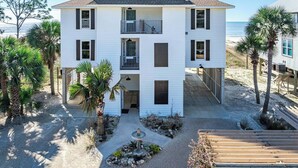 Ein zweistöckiges weißes Gebäude mit Balkon, umgeben von Palmen und einem Sandstrand.
