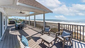 Eine überdachte Terrasse mit Gartenmöbeln, einem Grill und Blick auf den Strand.
