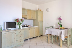 A kitchen with light wooden cabinets, a dining table with chairs, a TV, and a vase with flowers. - Two-room apartment of approximately 40 m2 composed of a living room with kitchenette, double sofa bed, double bedroom, bathroom, patio.Some apartments may also have a bunk bed.Endowed of:- TV- Outdoor chairs, table- External parking space- Kitchenette- A (Badesi)