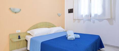 A bedroom with a bed, a nightstand, a wall-mounted light, and a window with curtains.