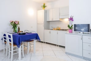 A compact kitchen with white cabinets, a dining table with a blue tablecloth, and a TV on the counter.