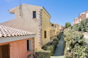 A narrow street with buildings on either side, featuring a mix of architectural styles, including a building with a stone column and a tiled roof.