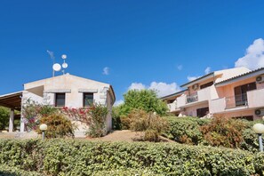 A building with a stone facade, a covered patio, and a garden with various plants and flowers. - Two-room apartment of approximately 40 m2 composed of a living room with kitchenette, double sofa bed, double bedroom, bathroom, patio.Some apartments may also have a bunk bed.Endowed of:- TV- Outdoor chairs, table- External parking space- Kitchenette- A (Badesi)