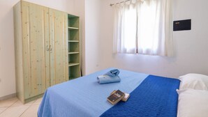 A bedroom with a bed, a wardrobe, and a window with curtains. - Two-room apartment of approximately 40 m2 composed of a living room with kitchenette, double sofa bed, double bedroom, bathroom, patio.Some apartments may also have a bunk bed.Endowed of:- TV- Outdoor chairs, table- External parking space- Kitchenette- A (Badesi)