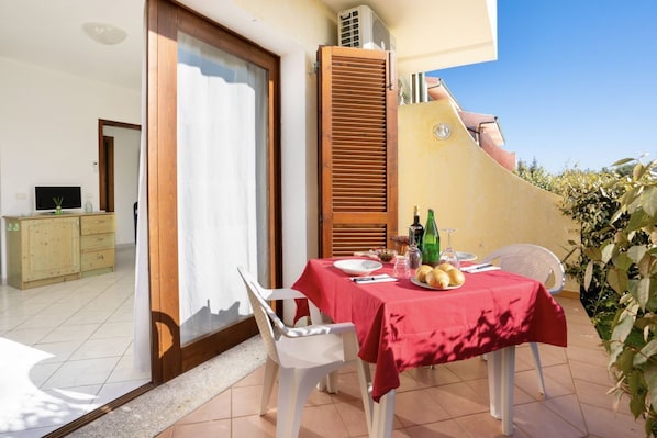 A balcony with a table set for two, a wooden shutter, and a TV in the background.