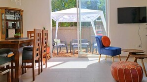Un salon doté d’une porte vitrée donnant sur une terrasse extérieure, d’un téléviseur fixé au mur et d’un meuble en bois contenant de la verrerie.