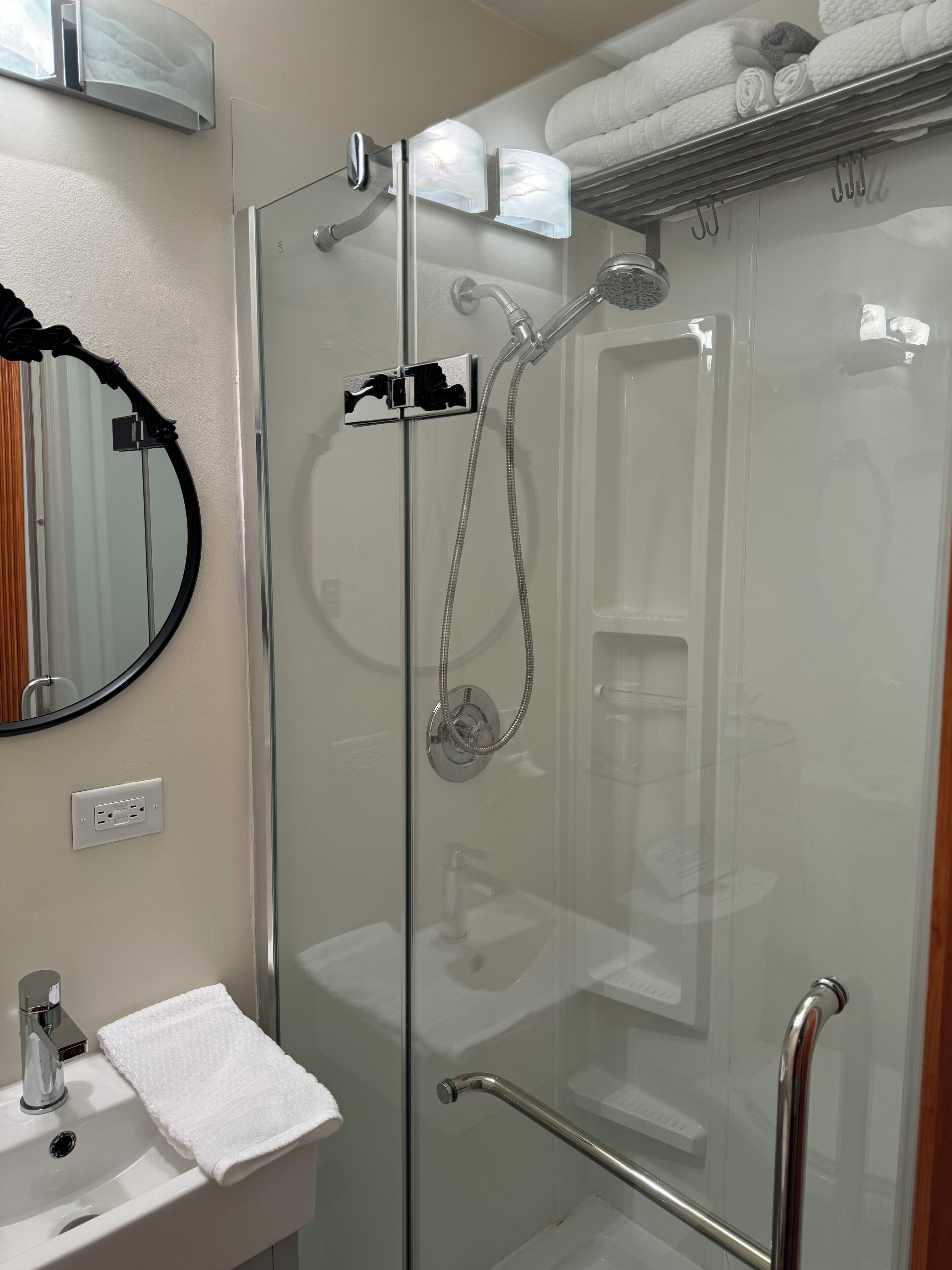 Uma casa de banho moderna com chuveiro em vidro, lavatório branco e porta-toalhas.
