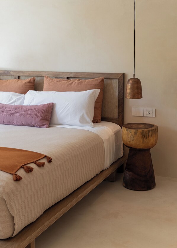 A neatly made bed with a wooden headboard, a bedside table with a wooden base, and a hanging pendant light. - Aflora Tulum (Tulum)