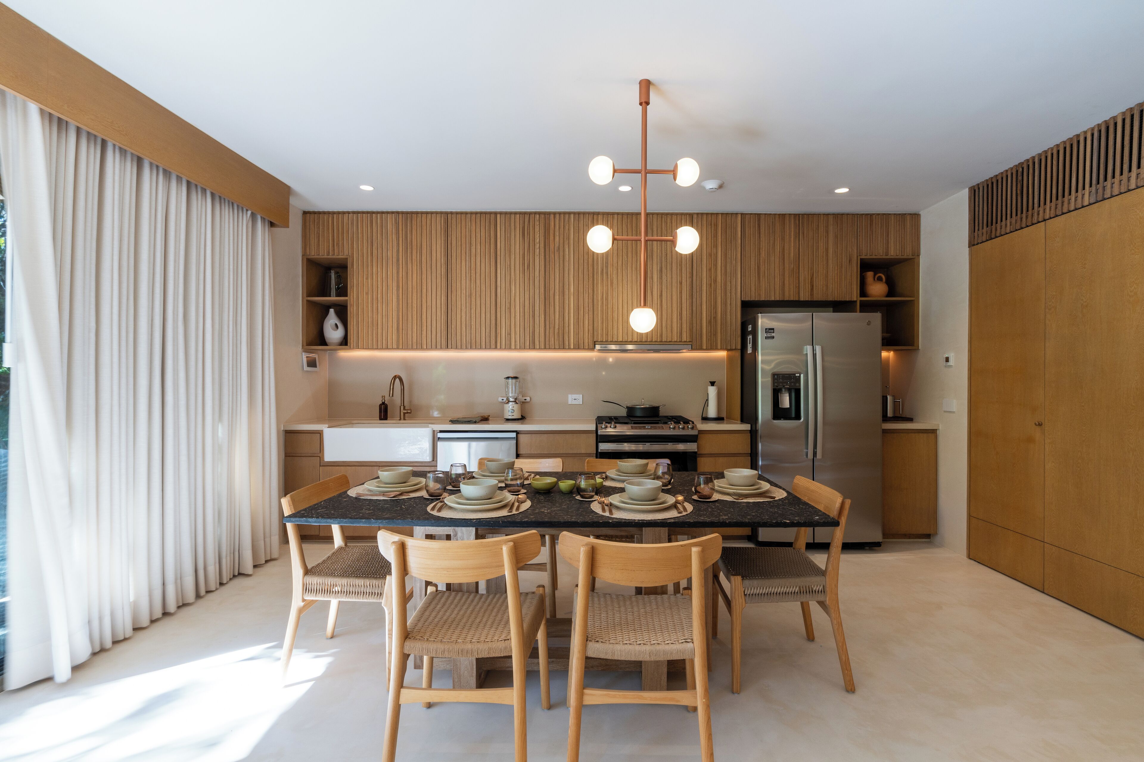 Una cucina moderna con mobili in legno, un'isola centrale e un'area pranzo con tavolo imbandito per quattro persone.