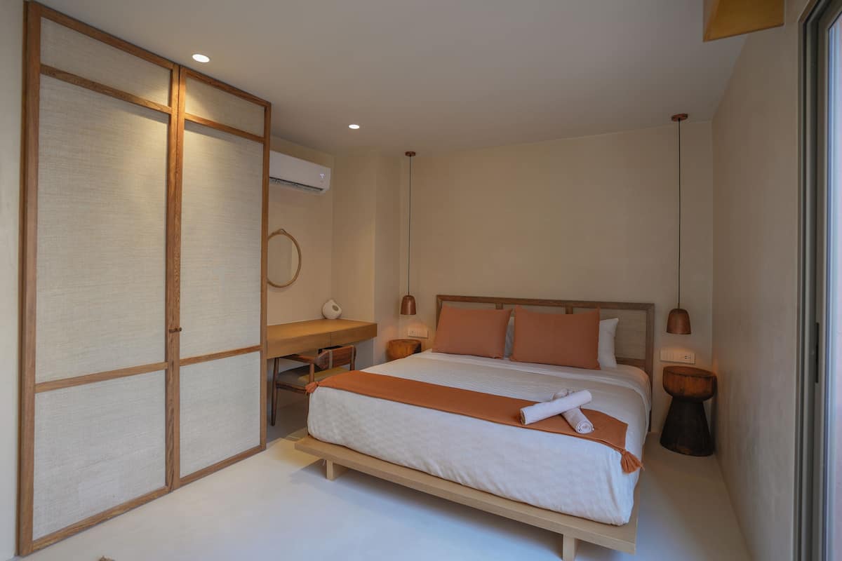 Quarto com cama, mesas de cabeceira, escrivaninha e uma grande porta deslizante.