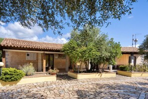 A courtyard with stone paving, a building with a tiled roof, and potted plants.