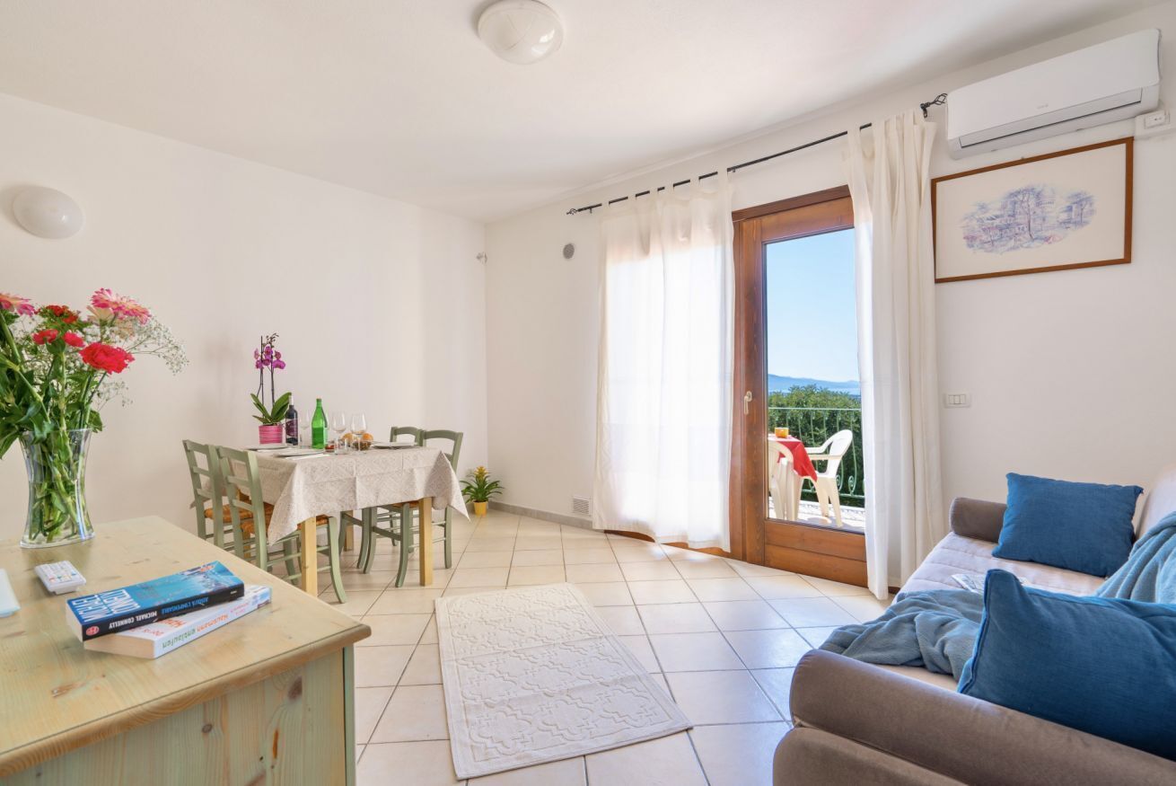 Un soggiorno con divano, un tavolo da pranzo con sedie, un angolo cottura e un balcone con vista.