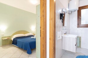 A bedroom with a bed, a nightstand, and a bathroom with a sink and mirror.