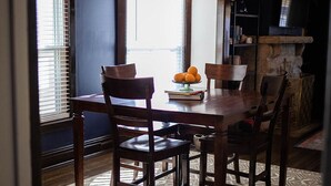 A dining area with a wooden table and chairs, a chandelier, and a fruit bowl on the table.