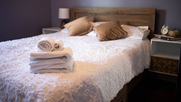 A neatly made bed with a fluffy white blanket, a stack of folded towels, and two beige pillows.