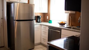 A kitchen with white cabinets, a stainless steel refrigerator, a coffee maker, and a sink.