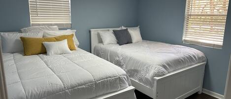 A bedroom with two single beds, white bedding, and a blue wall.